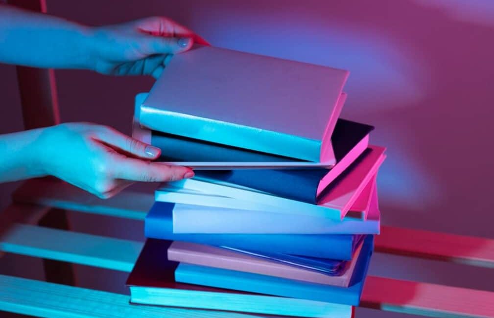 Hands exchanging a stack of colorful books under neon lights