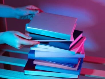Hands exchanging a stack of colorful books under neon lights