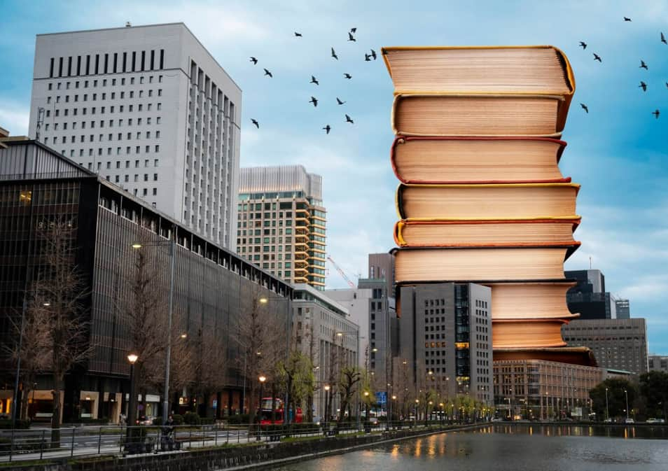 A towering stack of large books set against an urban cityscape