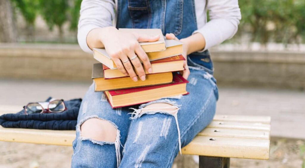 A person sitting on a bench holding a stack of hardcover books