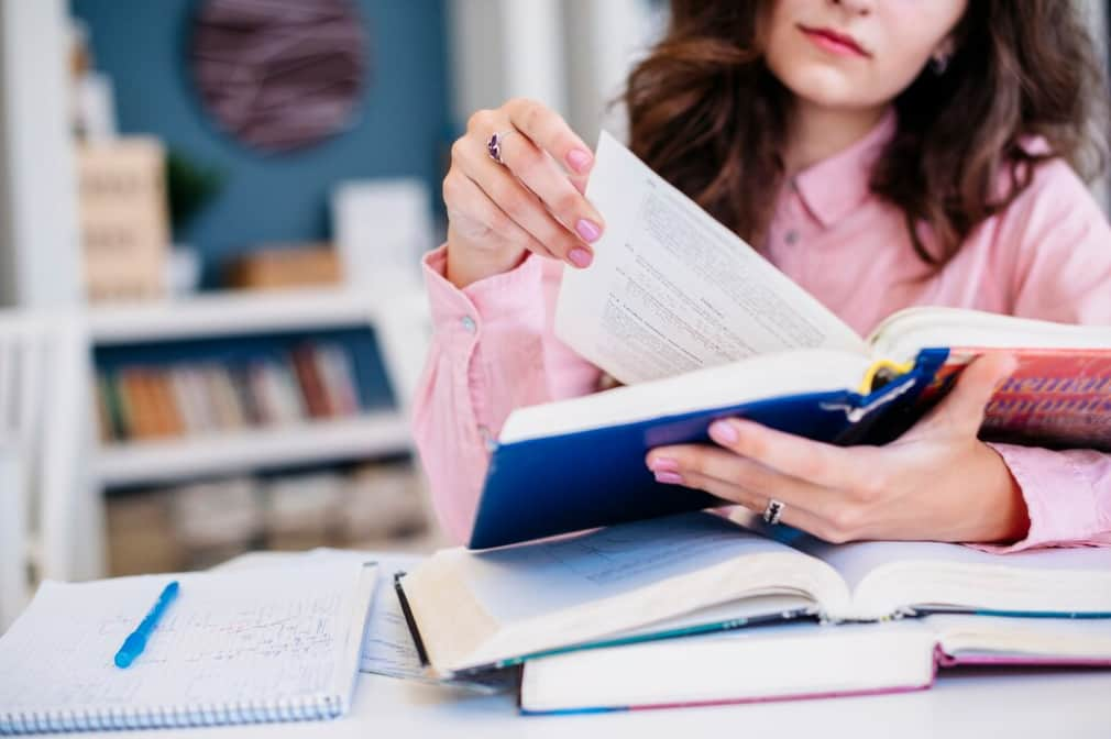 Close-up of a person reading a book with notes and a laptop nearby