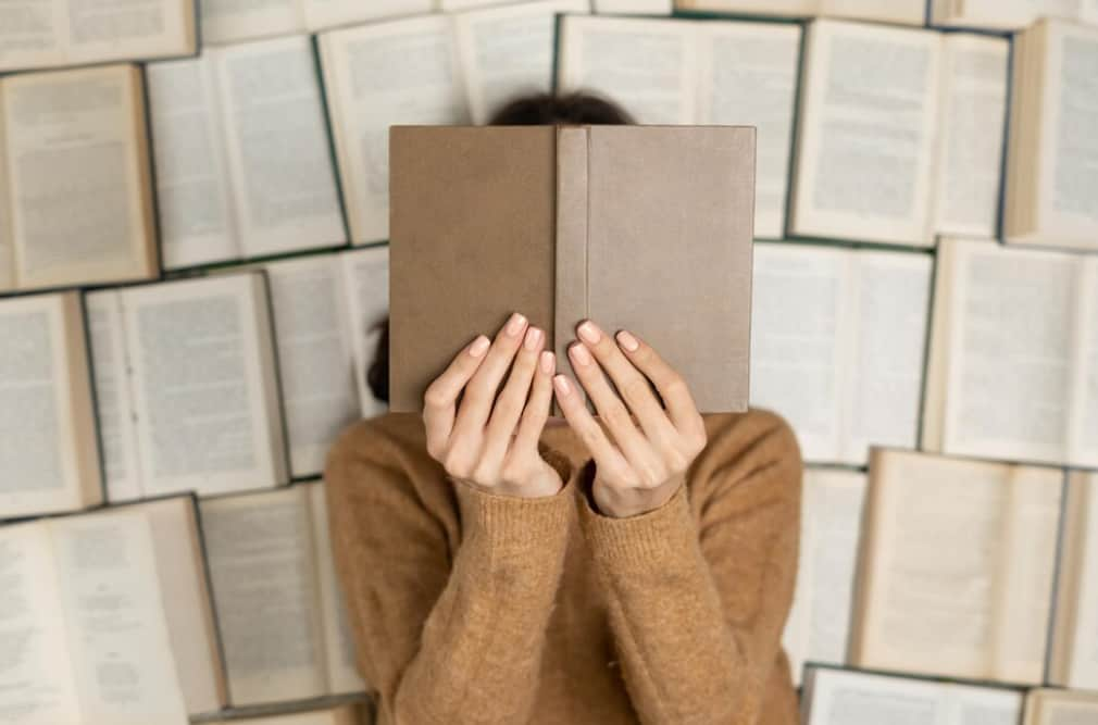 Person hidden behind an open book against a backdrop of books