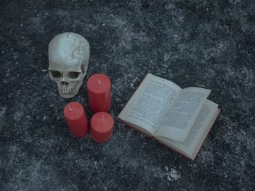 An open book lies near 3 candles and a skull