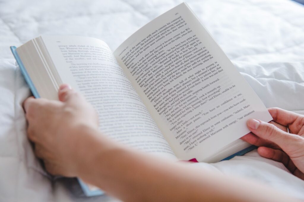 Close up of arms with open book on bed