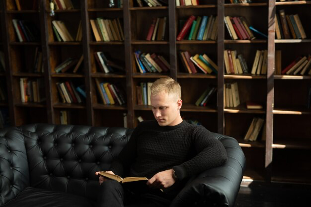 Man reading a book on a sofa in the library