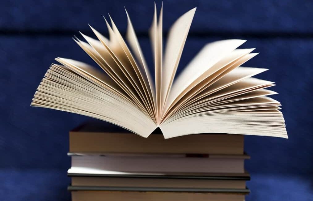 An open book on top of a stack against a blue backdrop