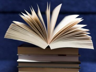 An open book on top of a stack against a blue backdrop